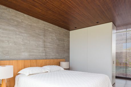 Minimalist bedroom with concrete walls, wood paneling, and built-in wardrobe.