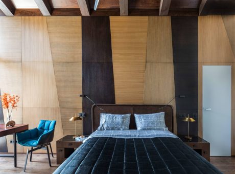 Minimalist bedroom with warm-toned wood paneling, textured quilted bedding, and sleek lighting.