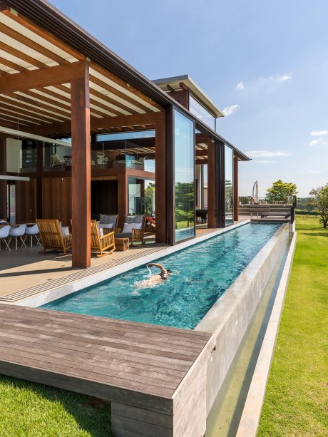 A modern, open-concept home with a wooden exterior, expansive windows, and an infinity pool.
