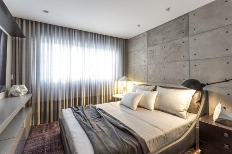 Minimalist bedroom with concrete walls, plush bedding, and soft lighting accents.