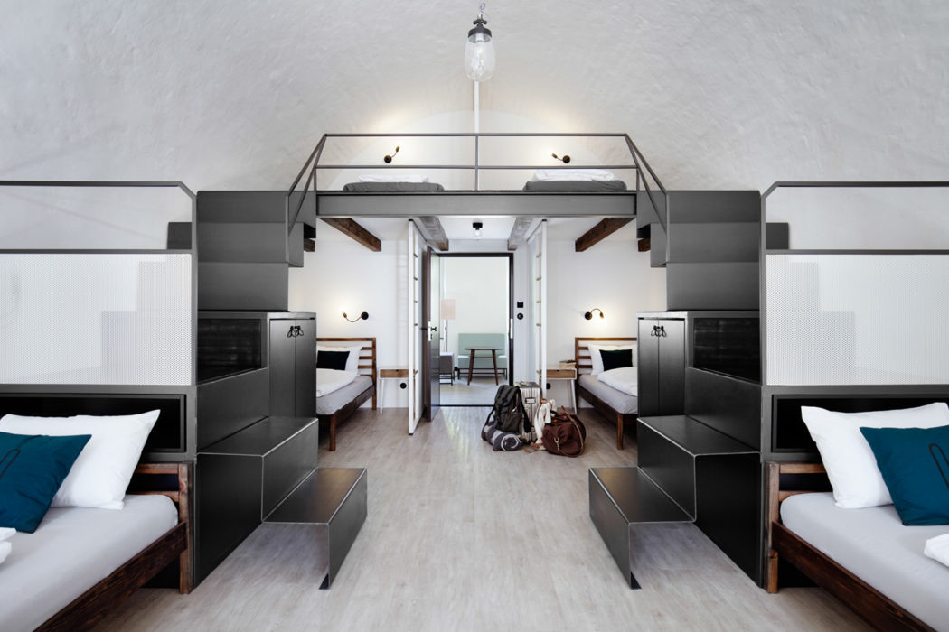 Minimalist, industrial-inspired hotel room with bunk beds, modern furnishings, and neutral palette.