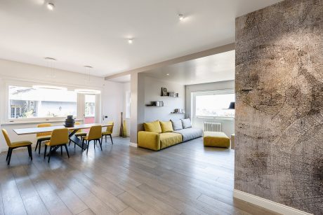 Bright, open-plan living area with gray hardwood floors, yellow sofa, and textured accent wall.