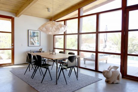 A modern dining room with wooden beams, large windows, and a sleek light fixture.
