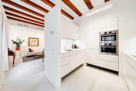 Bright, modern kitchen with sleek white cabinetry, high-end appliances, and exposed wood beams.