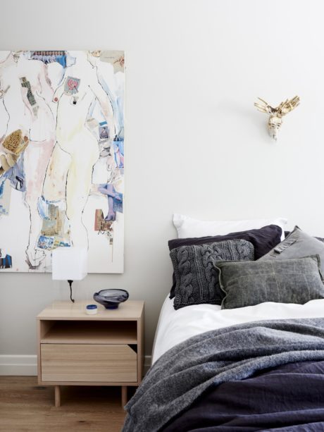 Minimalist bedroom with abstract artwork, cable-knit throws, and a wooden nightstand.