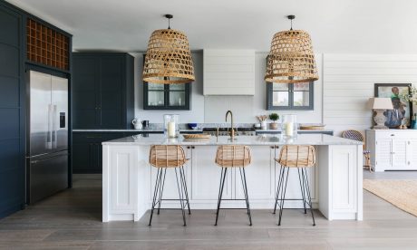 Spacious kitchen with dark cabinetry, white island, rattan pendant lights, and wood-toned barstools.
