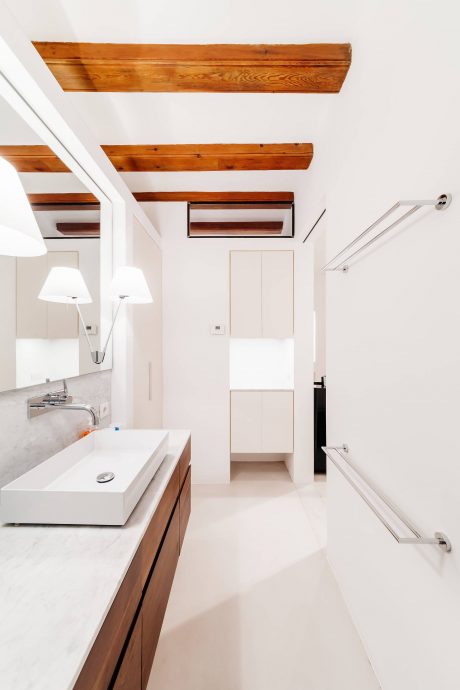 A modern bathroom with a white vanity, wooden ceiling beams, and recessed lighting.