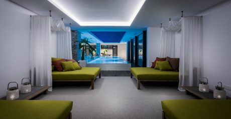 Chic modern interior with plush green sofas, pool, and dramatic lighting features.