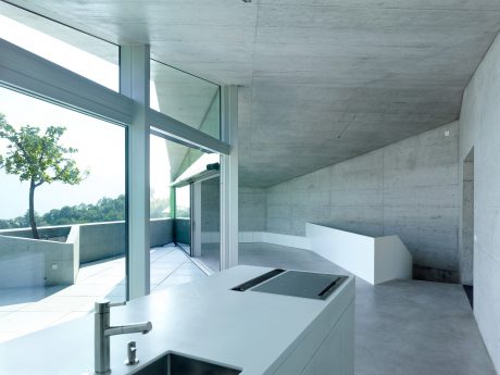 A modern, minimalist interior with concrete walls, floor, and ceiling, and large glass windows overlooking nature.