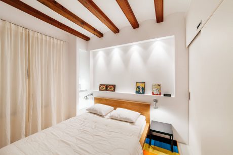Cozy bedroom with exposed wooden beams, white walls, and minimalist decor.