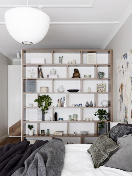 A cozy bedroom with a large, wooden shelving unit displaying decor and plants.