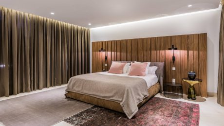 Spacious bedroom with warm wood paneling, plush bedding, and modern lighting fixtures.