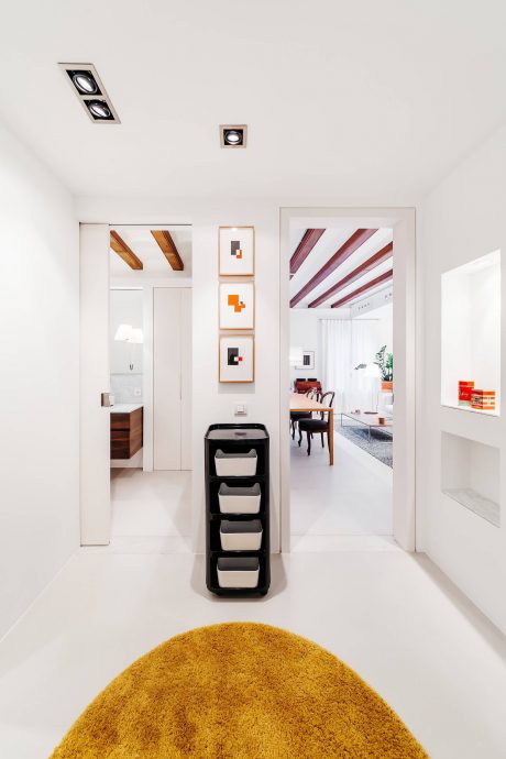 Modern interior with sleek white walls, geometric lighting, and vibrant yellow rug.