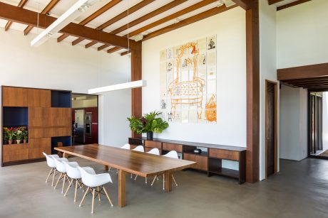 A modern and minimalist dining room with wooden beams, sleek furniture, and an abstract mural.
