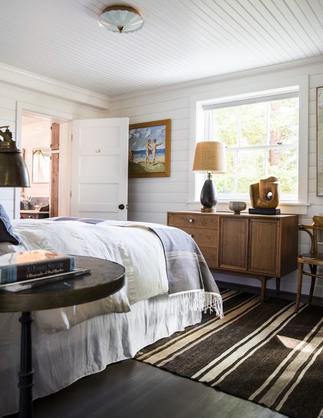 Cozy bedroom with wood-paneled walls, vintage furniture, and striped area rug.