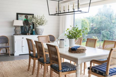 A modern farmhouse-style dining room with a rustic wooden table, cane-back chairs, and a statement light fixture.