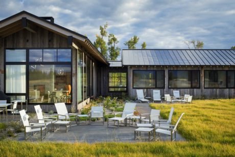 Rustic cabin with modern glass facade, expansive outdoor patio, and lush greenery.