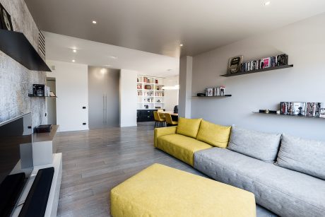 Contemporary open-plan living space with gray sofa, yellow accents, and built-in shelves.