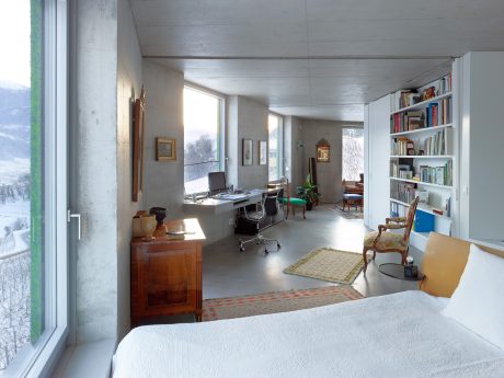 Cozy concrete home office with built-in bookshelves, large windows, and warm furnishings.