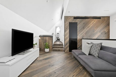 Modern, minimalist living room with wood-paneled accent wall, gray couch, and TV console.