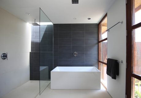 Contemporary bathroom with sleek black tiles, glass shower enclosure, and freestanding white tub.