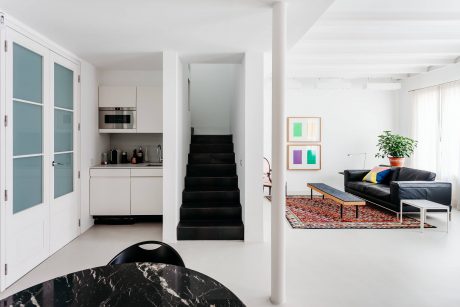 Minimalist living space with modern kitchen, monochrome staircase, vibrant artwork.