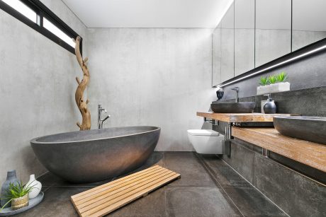 A modern bathroom with a concrete bathtub, wooden vanity, and decorative accents.