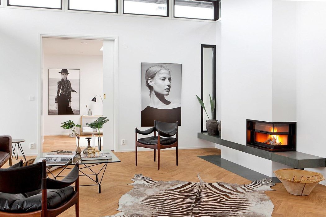 A modern living room with large windows, artwork, and a fireplace set against a clean, white backdrop.