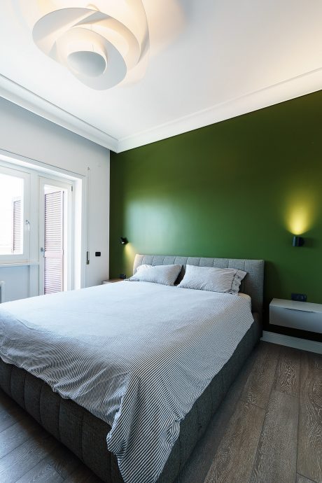 Minimalistic bedroom with contrasting green walls, sleek lighting, and a plush gray bed.