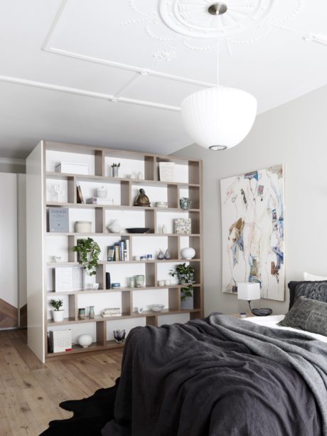 A modern bedroom with a large bookshelf, white walls, and a cozy gray blanket.