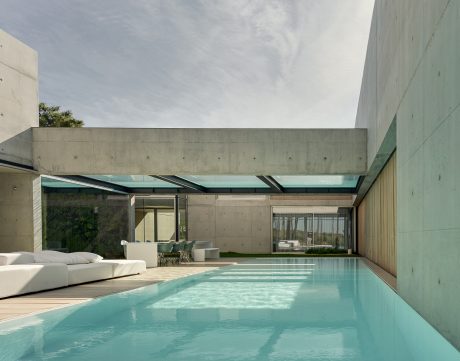 Minimalist outdoor living space with a concrete structure, glass roof, and inviting pool.