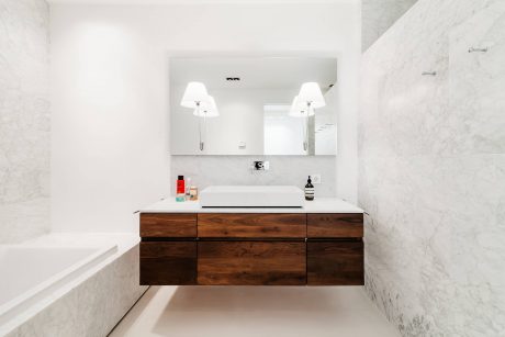 A modern bathroom with a floating wood vanity, double sinks, and marble walls.