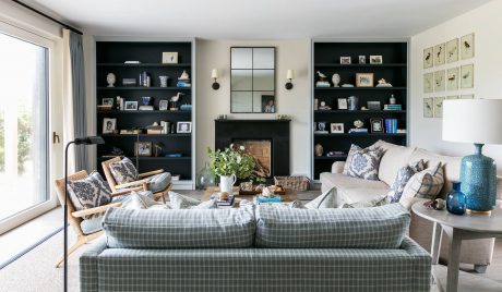 Cozy living room with built-in bookcases, fireplace, and plaid sofa amidst rustic decor.