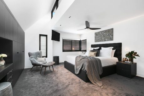 A modern bedroom with black and white decor, a plush gray armchair, and a ceiling fan.