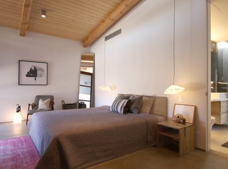 Cozy bedroom with wooden ceiling, neutral bedding, and decorative lighting fixtures.