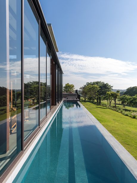 A modern glass-walled building with a long, narrow pool reflecting the lush surrounding trees.