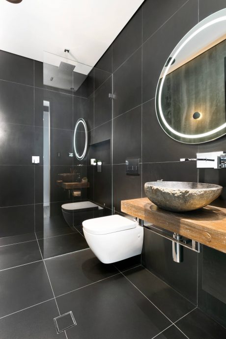 Sleek bathroom design with dark tile, modern sink, and illuminated circular mirror.