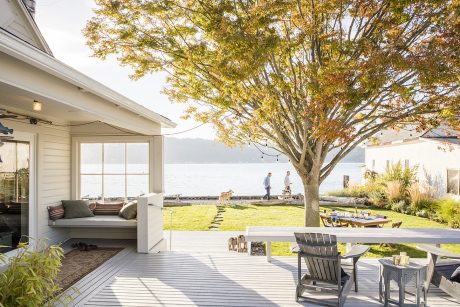 A cozy lakeside deck with a covered seating area, surrounded by vibrant autumn foliage.