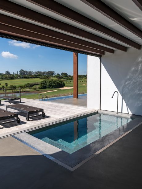 A modern, open-air patio with an infinity pool and lush green scenery beyond the glass walls.