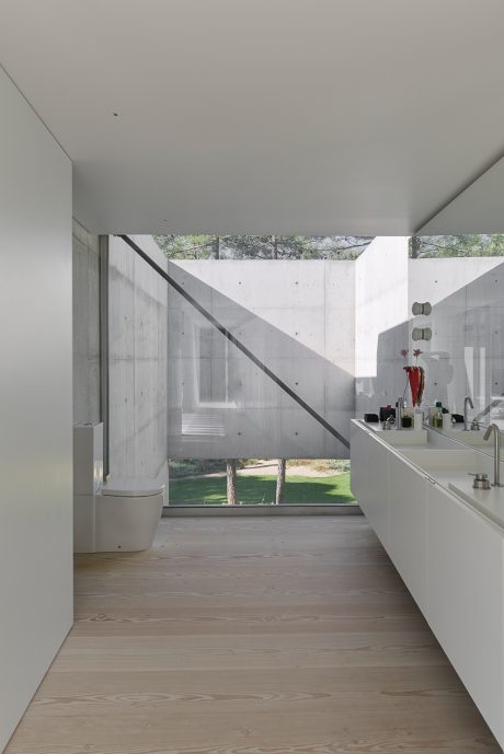 A modern, minimalist interior with concrete walls, large windows, and a wooden floor.
