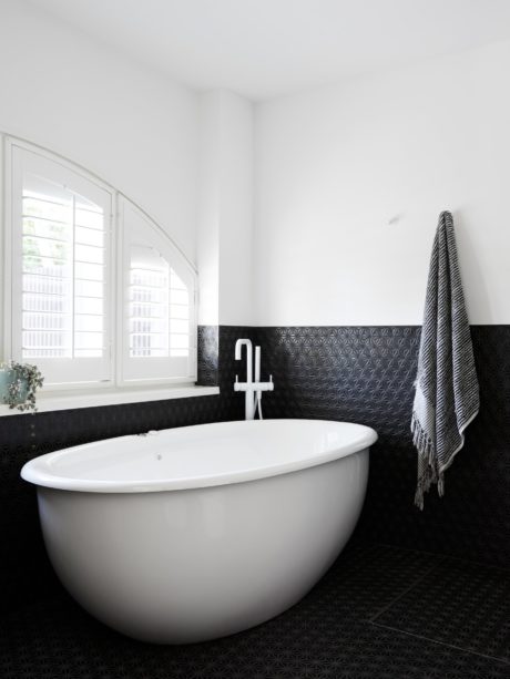 Bright bathroom with large oval tub, patterned black tiles, and arched windows.
