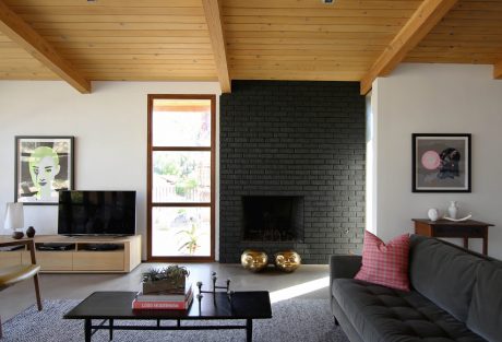 Cozy mid-century modern living room with wood-beamed ceiling, black brick fireplace.