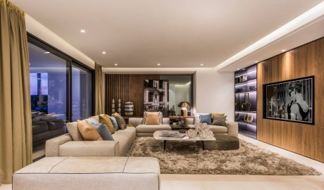 Spacious living room with plush seating, wood paneling, and scenic night cityscape view.