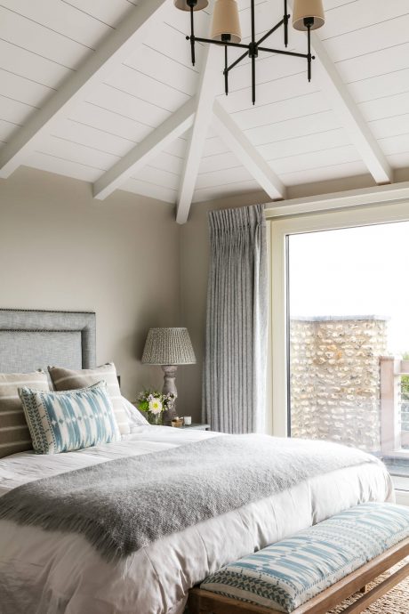 Cozy bedroom with a vaulted ceiling, wall-mounted sconces, and patterned bedding.
