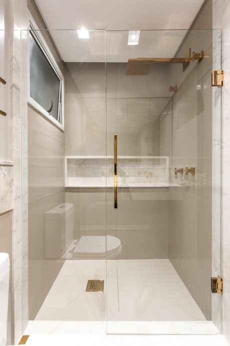 Minimalist bathroom design with glass enclosure, gold fixtures, and marble tile.