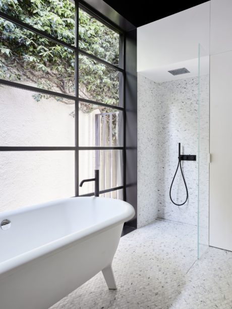 Minimalist bathroom design with freestanding tub, glass wall, and mosaic tile floor.