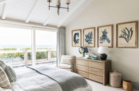 Cozy beach-inspired bedroom with vaulted ceiling, framed botanical art, and wood furniture.