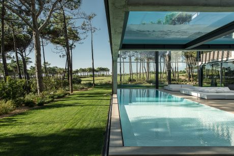 Sleek, modern home with large glass walls, reflecting pool, and lush, forested surroundings.