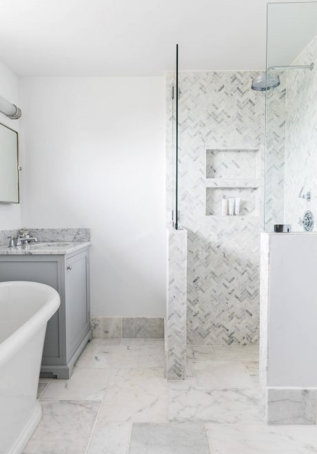 Bright, modern bathroom with marble tiling, gray vanity, and minimalist shower.