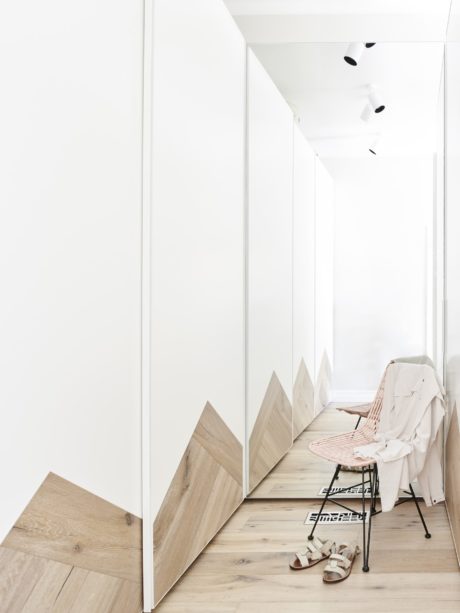 Modern, minimalist hallway with wooden accents and a small chair against a white wall.